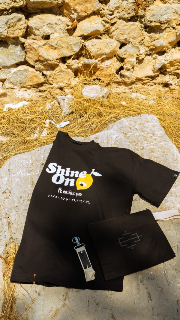 Φωτογράφιση της μπλούζας shine on χρώματος μάυρο σε συνδιασμό με το μαύρο τσαντάκι clutch και μπρελόκ σε χρώμα μπέζ